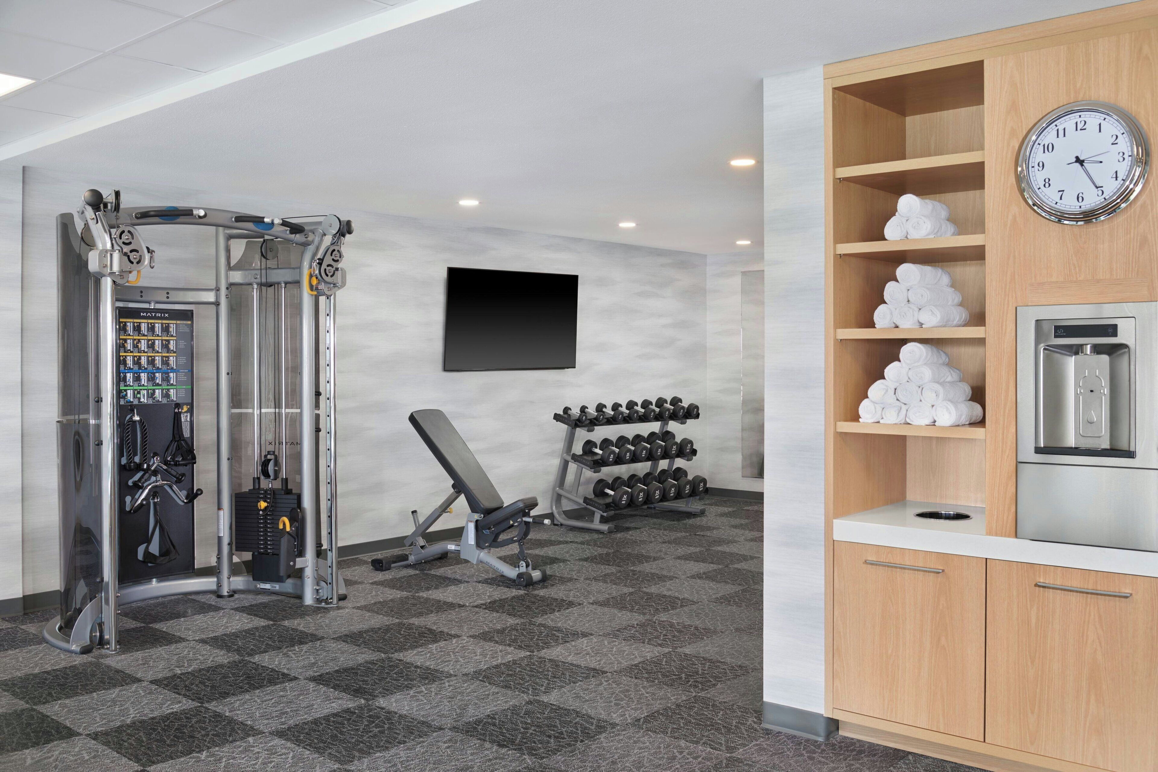 Une salle de sport équipée de matériel d’exercice, d’un banc, d’haltères et d’une horloge fixée au mur.