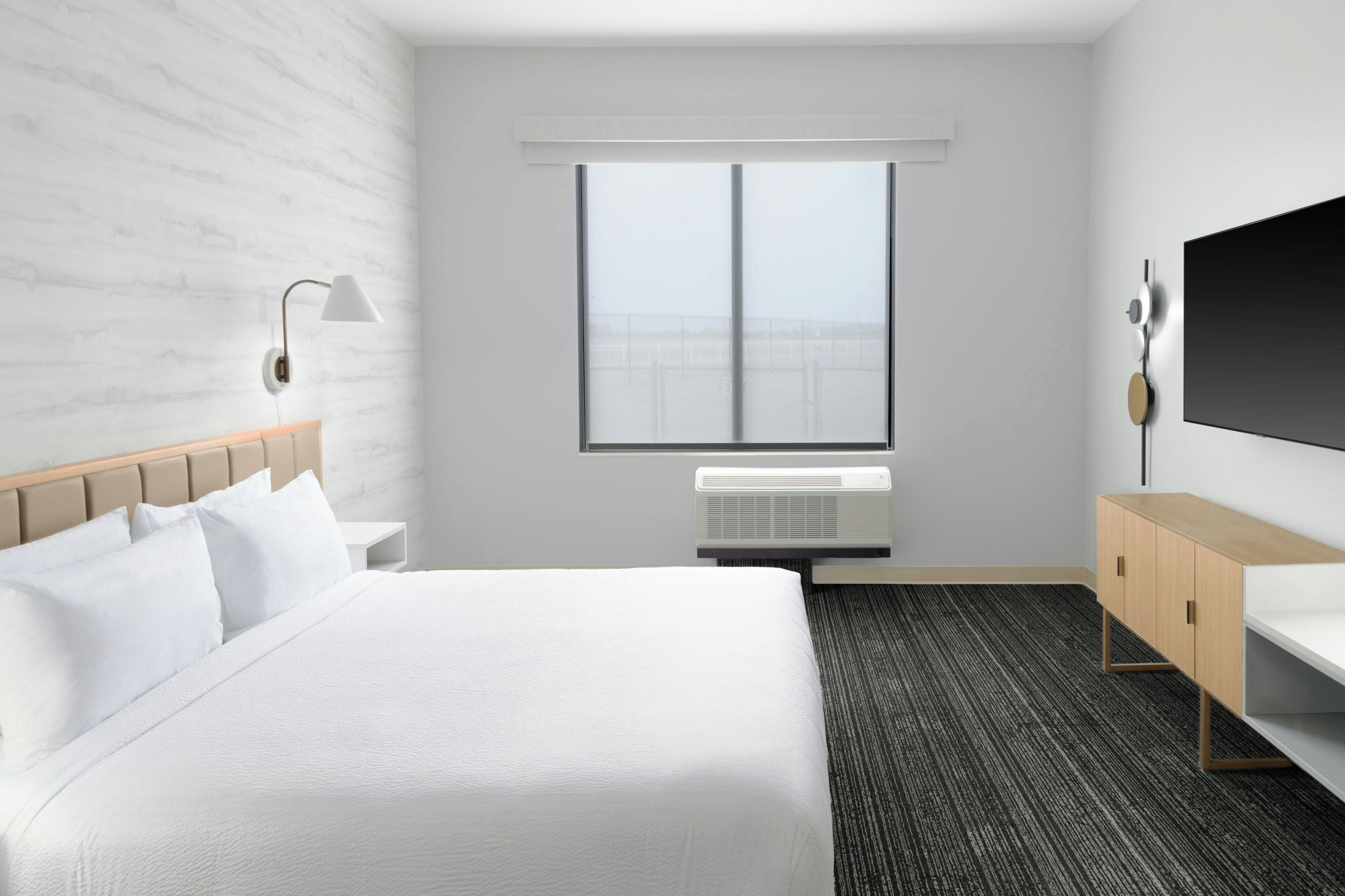 A hotel room with a large bed, a bedside table, a TV, and a window with a city view.