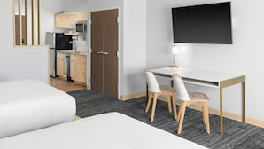 Una camera d'albergo moderna con un letto, una scrivania con sedia, una TV a schermo piatto, un angolo cottura e una porta che dà su un'altra stanza.