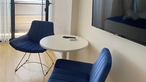 A room with two blue chairs, a small white table, a flat-screen TV mounted on the wall, and a view of a building through a glass door. - orbi city apartments (Batumi)
