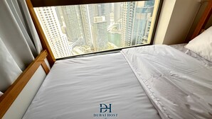 Ein Bett mit weißer Bettwäsche, einem Holzkopfbrett und einem Fenster mit Blick auf hohe Gebäude.