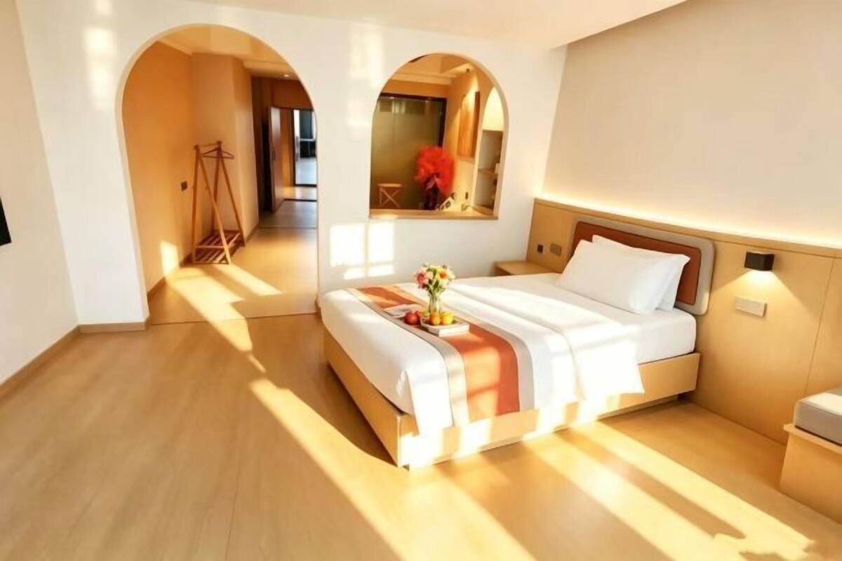 A hotel room with a bed, a bedside table, a mirror, and a view of the hallway.