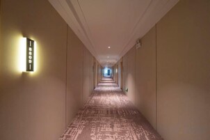 Un pasillo de hotel con piso alfombrado, luminarias fijadas a la pared y un largo camino hacia el final.