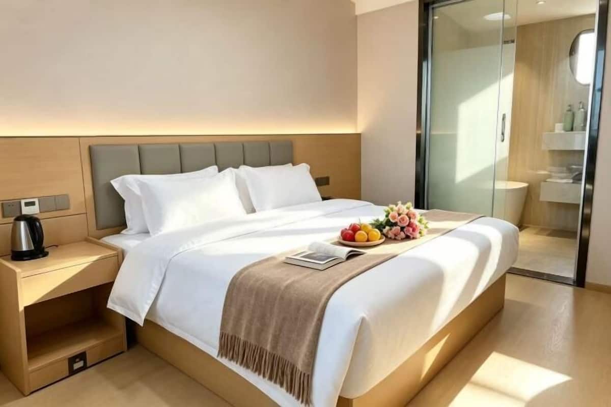 A hotel room with a bed, bedside table, and a glass door leading to a bathroom.