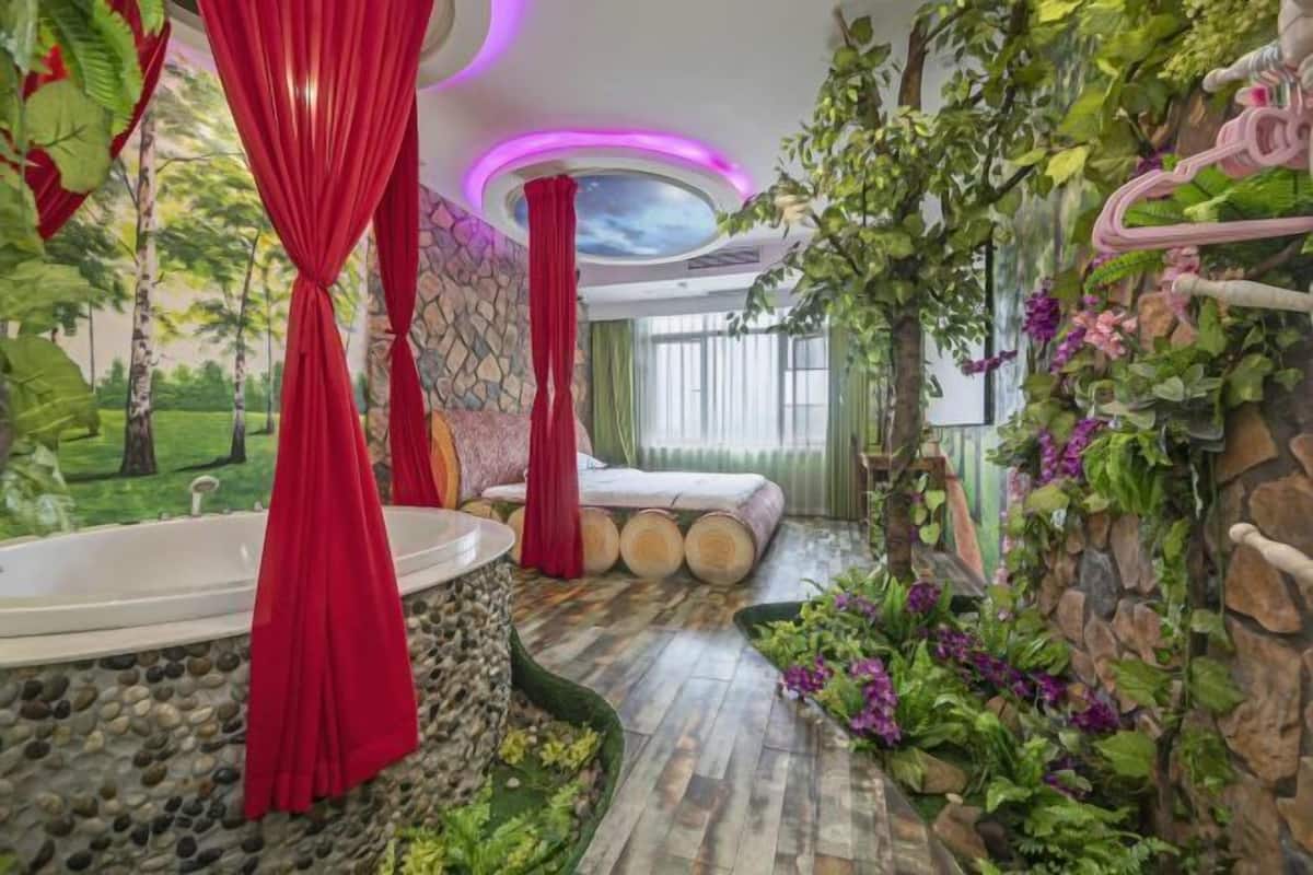 A room with a bathtub, a bed, and a stone wall with greenery.