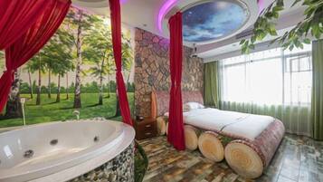 Ein Schlafzimmer mit einer großen Badewanne, einem Bett mit Holz-Kopfteil und einem Wandgemälde von Bäumen.
