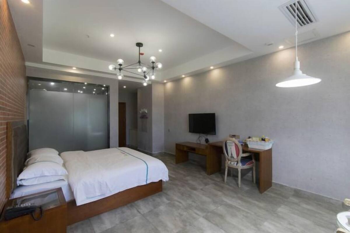A modern bedroom with a bed, a desk, a chair, and a TV.