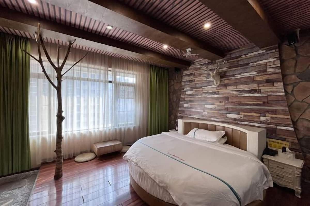 A bedroom with a bed, a stone wall, a wooden ceiling, and a window with curtains.