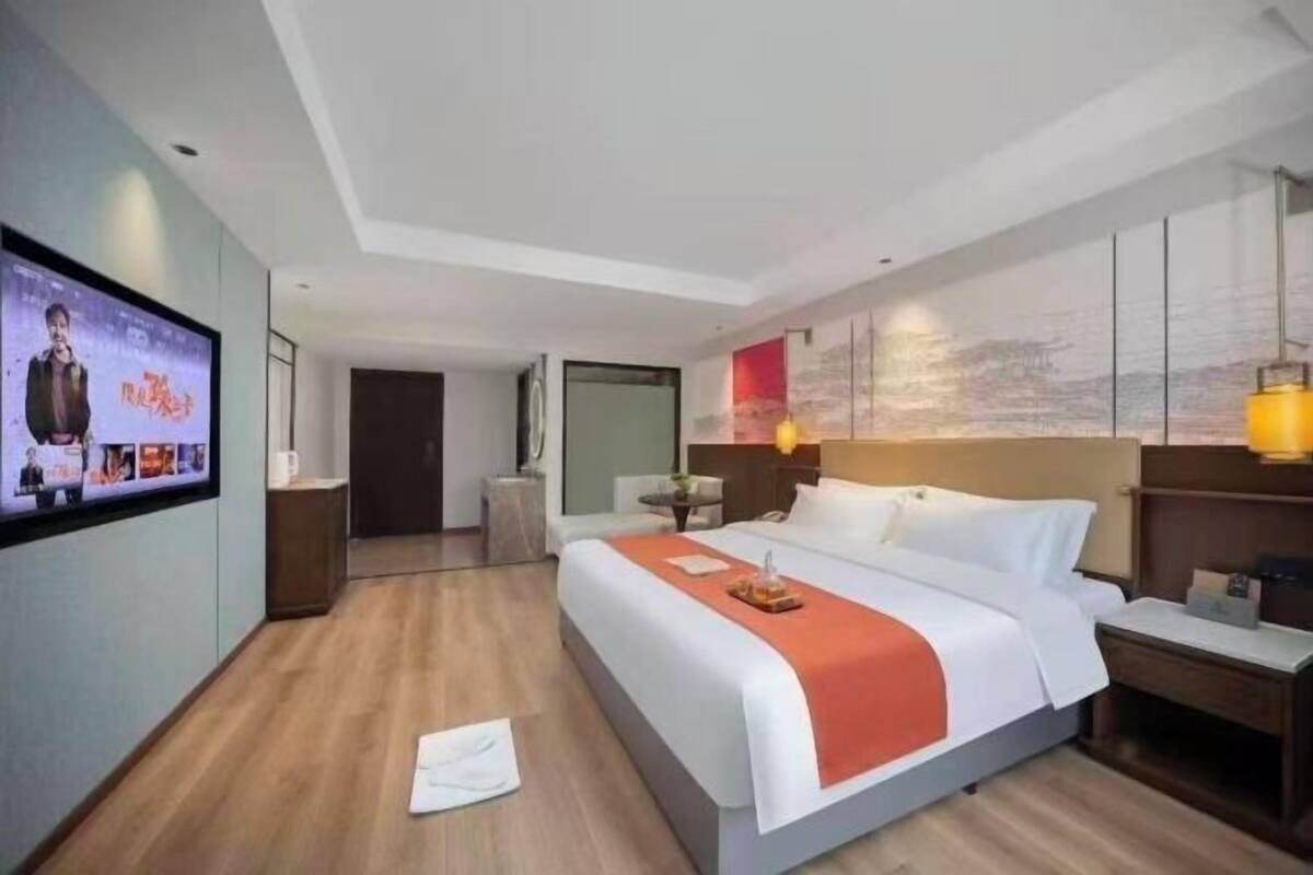 A modern hotel room with a large bed, a flat-screen TV, a desk, and a wall-mounted artwork.