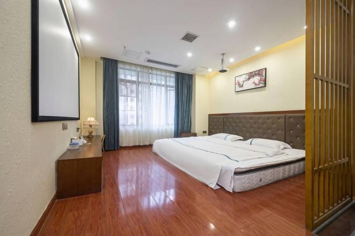 A hotel room with a large bed, a desk with a lamp, and a window with curtains.