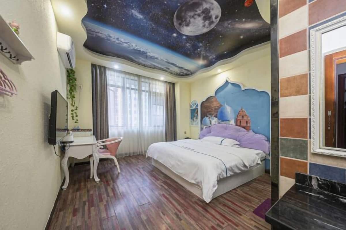 A bedroom with a bed, a desk, a chair, a mirror, and a wall with a mural.