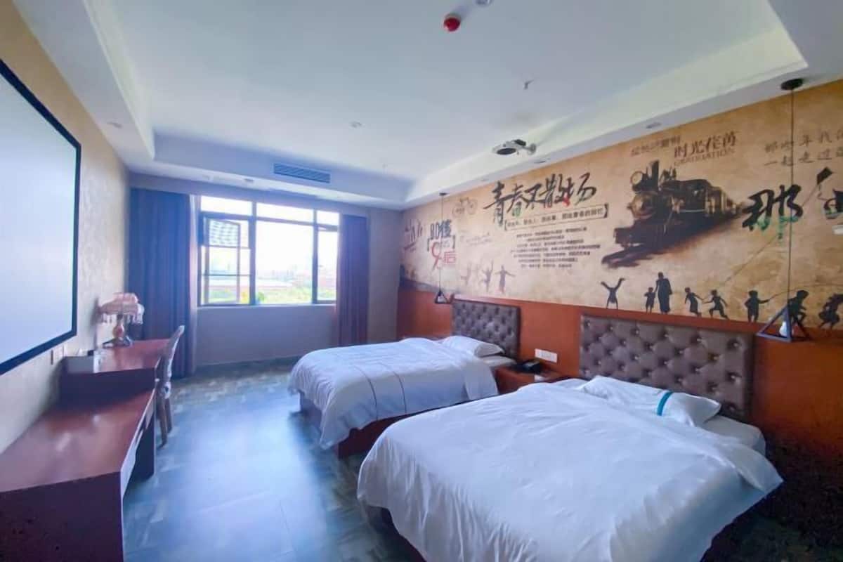 A hotel room with two beds, a desk, and a large window.
