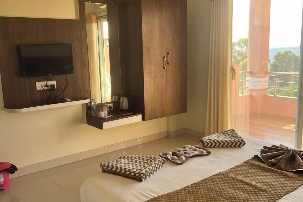 Quarto de hotel com cama grande, televisão na parede, armário de madeira e varanda com vista.
