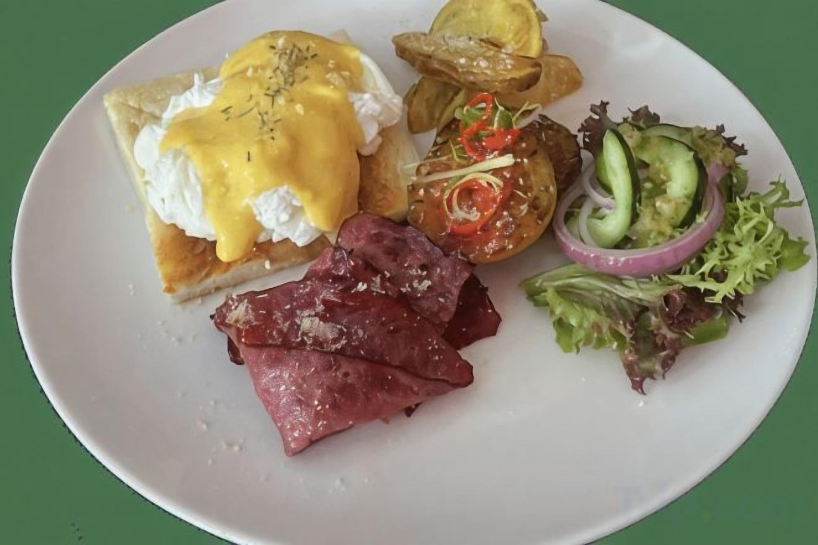 Een bord met Eggs Benedict, ham, chips en een salade.