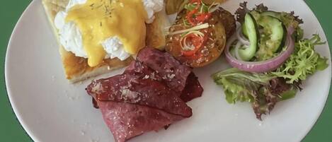 Een bord met Eggs Benedict, ham, chips en een salade.