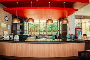 A hotel reception area with a wooden counter, pendant lighting, and a view of greenery outside. - 100 Sunset Kuta Hotel & Ballroom (Bali)