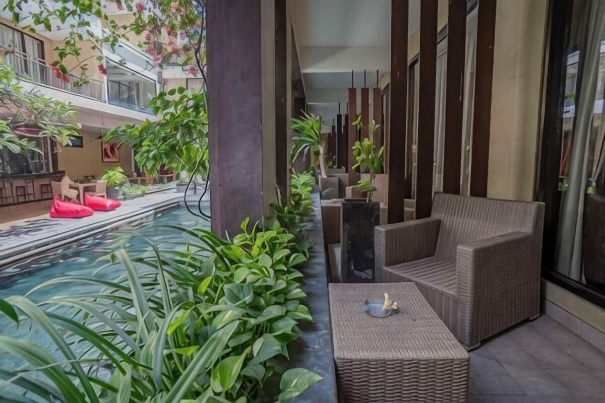 A pool area with a wicker sofa and a small table, surrounded by plants and a glass railing.