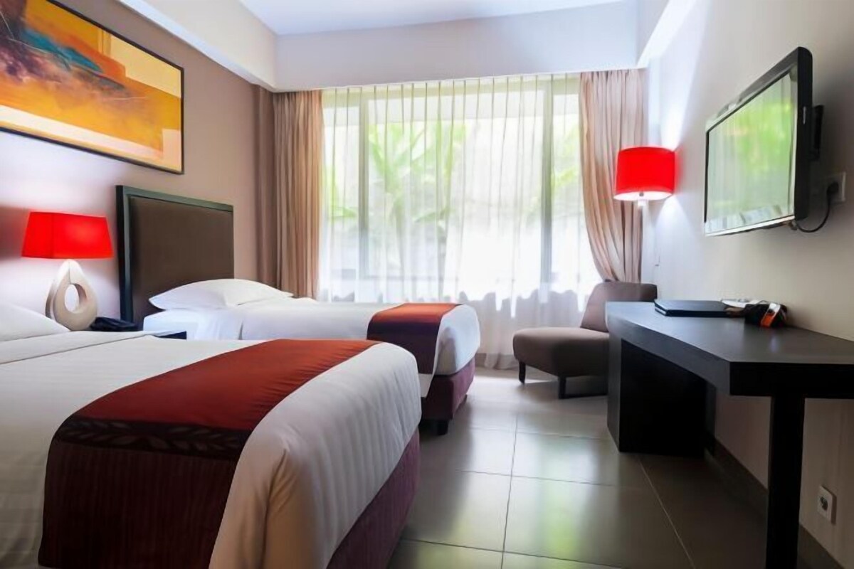 Ein Hotelzimmer mit zwei Betten, einem Schreibtisch, einem Stuhl, einem Fernseher und einem Fenster mit Vorhängen.