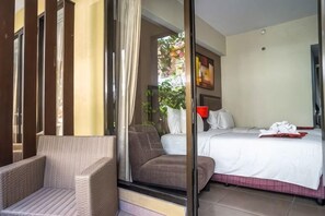 A hotel room with a bed, a chair, and a view through a glass door. - 100 Sunset Kuta Hotel & Ballroom (Bali)