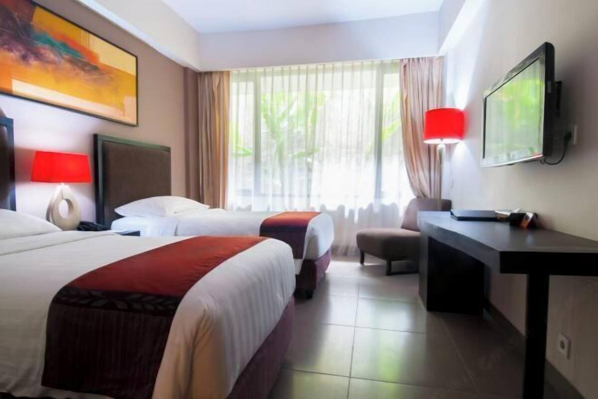Ein Hotelzimmer mit zwei Betten, einem Schreibtisch, einem Fernseher und einem Fenster mit Vorhängen.