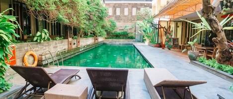 A pool area with lounge chairs and a small table, surrounded by greenery and a brick wall.