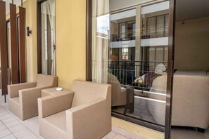 A balcony with wicker furniture and a glass door leading to a room. - 100 Sunset Kuta Hotel & Ballroom (Bali)