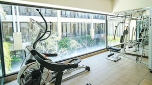A gym with exercise equipment, large windows, and a view of buildings. - 100 Sunset Kuta Hotel & Ballroom (Bali)
