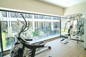 A gym with exercise equipment, large windows, and a view of buildings. - 100 Sunset Kuta Hotel & Ballroom (Bali)