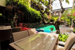 An outdoor seating area with wicker furniture, a pool, and lush greenery. - 100 Sunset Kuta Hotel & Ballroom (Bali)