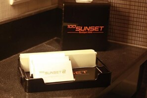 A hotel reception desk with a black box labeled "100 SUNSET" and a black tray with papers.