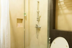Un baño con cabina de ducha de vidrio, inodoro y un estante pequeño con artículos de aseo.