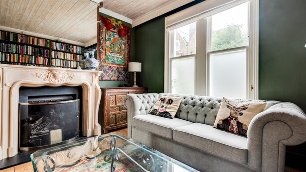 Una sala de estar acogedora con chimenea, un sofá con cojines decorativos, una estantería y un tapiz colorido.