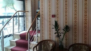 A staircase with red carpeted steps leading to a landing area with patterned wallpaper and two wooden chairs.