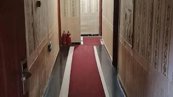A hallway with a red carpet, wooden walls, and a fire extinguisher on the right.