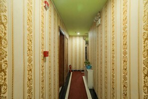 Un pasillo con papel tapiz estampado, alfombra roja y una puerta al final.