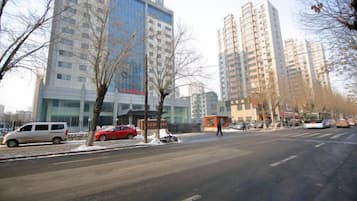 Una calle flanqueada por edificios altos, coches aparcados y árboles sin hojas.