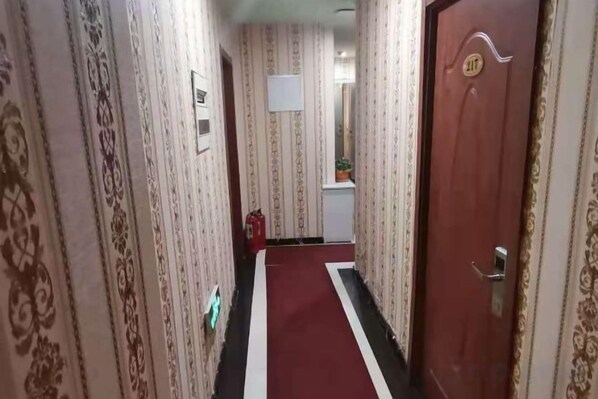 Un pasillo con papel tapiz estampado, alfombra roja y una puerta con la leyenda '217'.