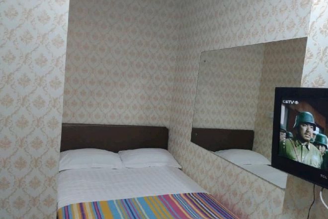 Un lit simple avec une couverture à rayures, un téléviseur fixé au mur et un papier peint à motifs.