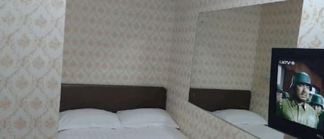 A single bed with a striped blanket, a television on the wall, and patterned wallpaper.