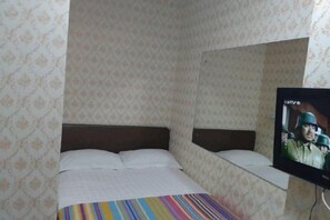 A single bed with a striped blanket, a television on the wall, and patterned wallpaper.