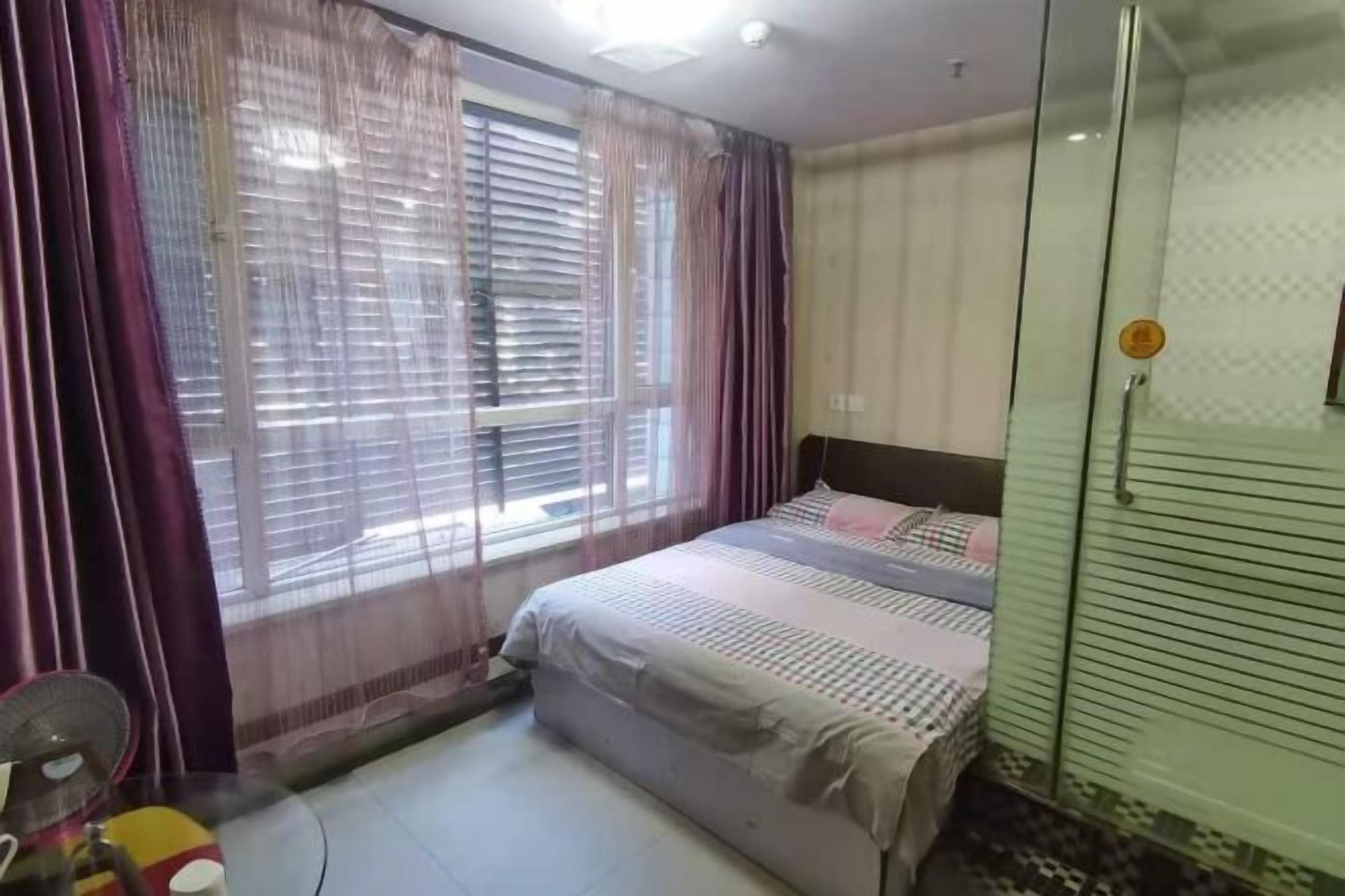 A bedroom with a bed, a window with curtains, a fan, and a wardrobe.