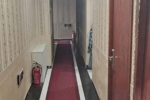 Un pasillo estrecho con alfombra roja, un extintor y una puerta a la derecha.