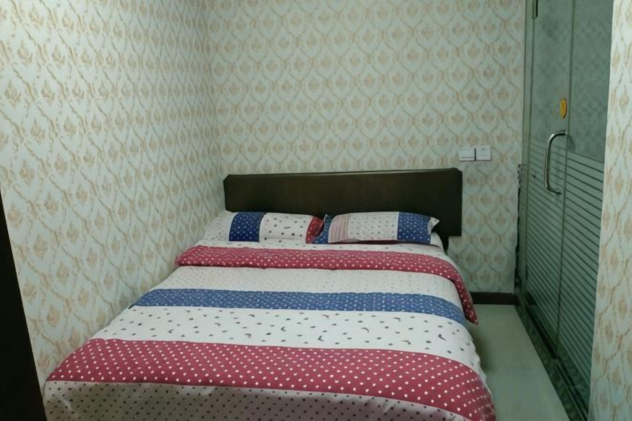 A room with a bed, patterned wallpaper, and a green door.