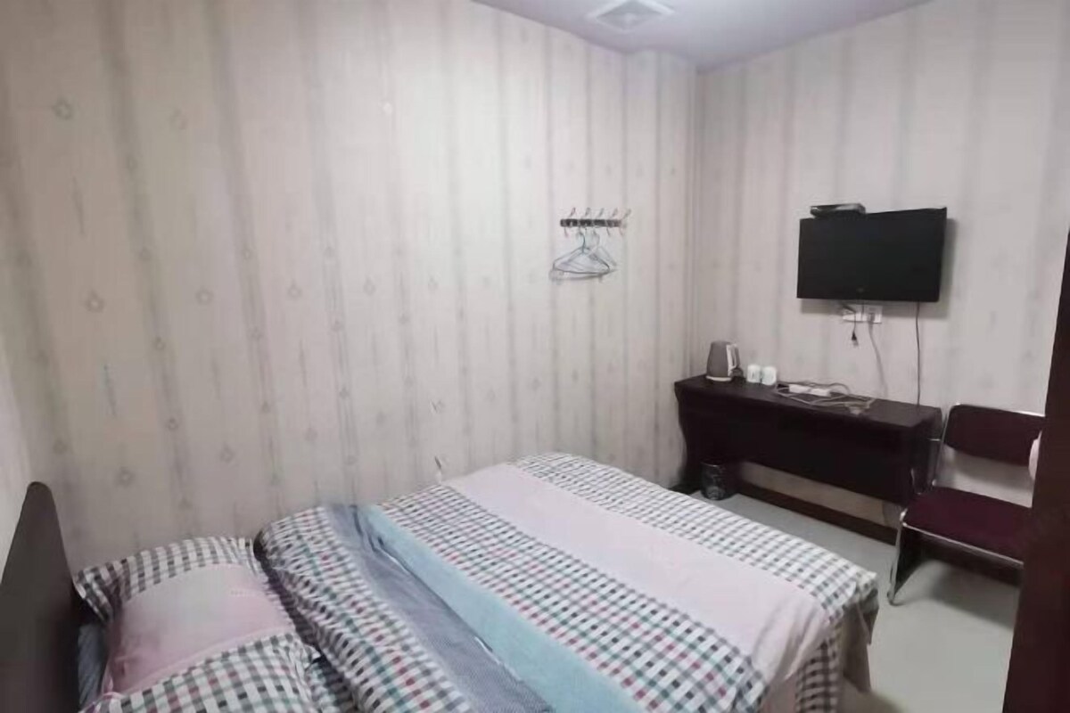 Quarto com cama, escrivaninha, cadeira, televisão e cabideiro.