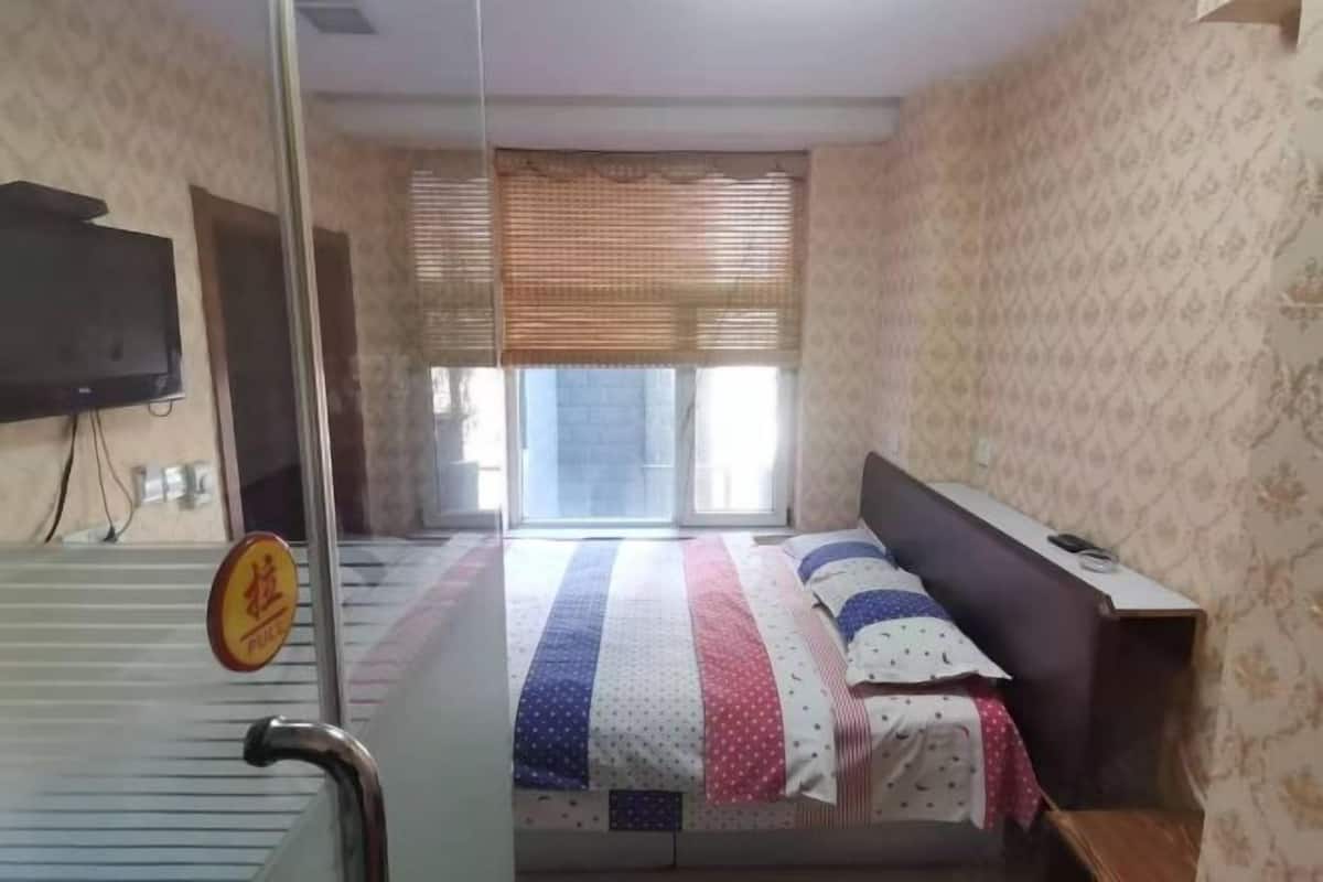 A bedroom with a bed, a television on the wall, a window with blinds, and a pull sign on the door.