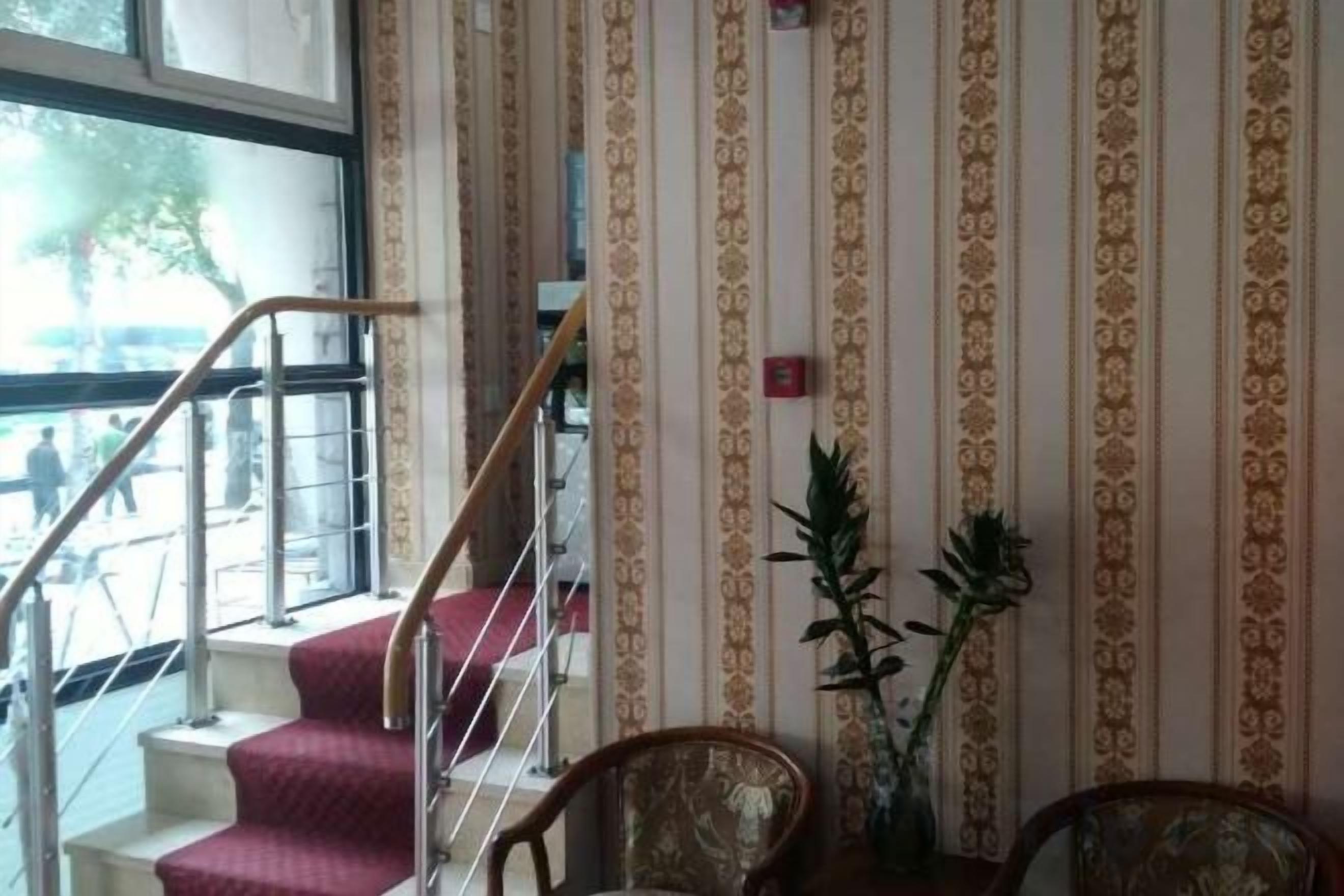 A staircase with a handrail leading to an upper floor, a patterned wall, and two chairs with a potted plant.
