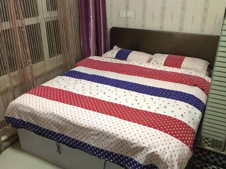 A bed with a striped bedspread, a headboard, and a window with curtains.