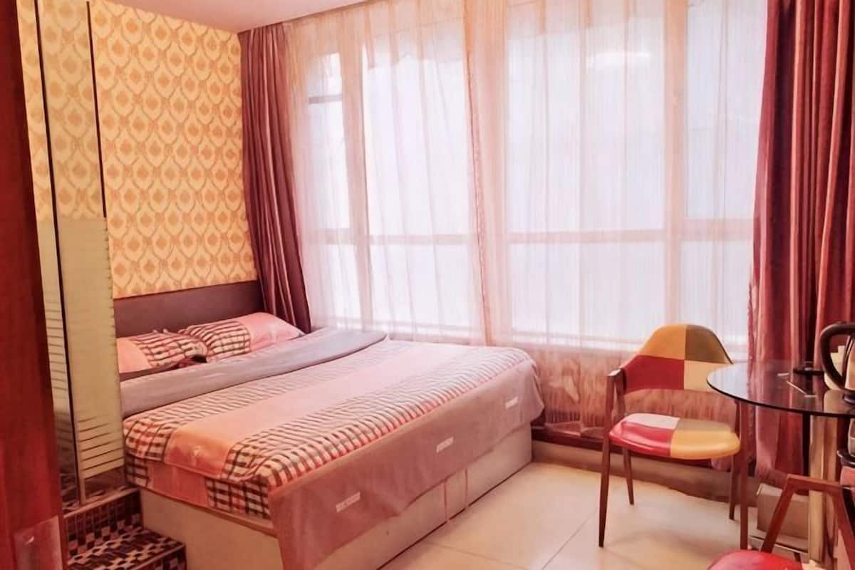 A bedroom with a bed, a chair, a small table, and a window with curtains.