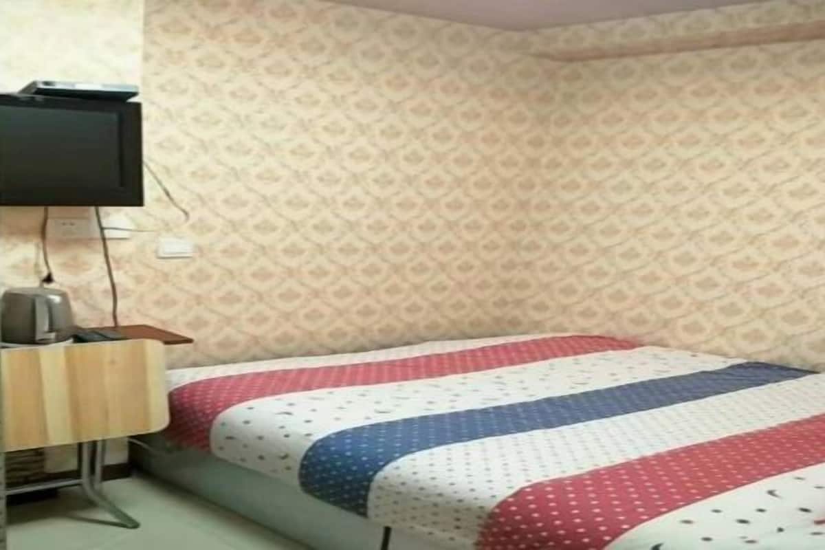 A small room with a bed, a desk, a television, and patterned wallpaper.