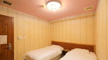 A room with two beds, a wooden door, and a ceiling light fixture.